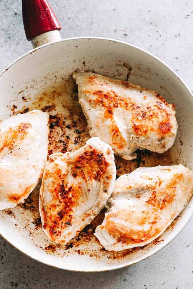 Searing chicken breasts in a skillet.