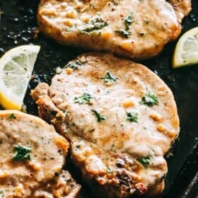 Three fully cooked pork chops on a sheet pan surrounded by lemon slices.