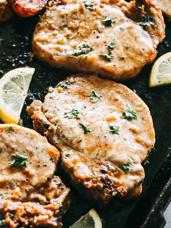 Three fully cooked pork chops on a sheet pan surrounded by lemon slices.