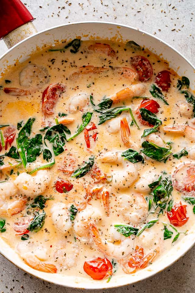 A skillet with Cream Sauce, cherry tomatoes, baby spinach, and shrimp.