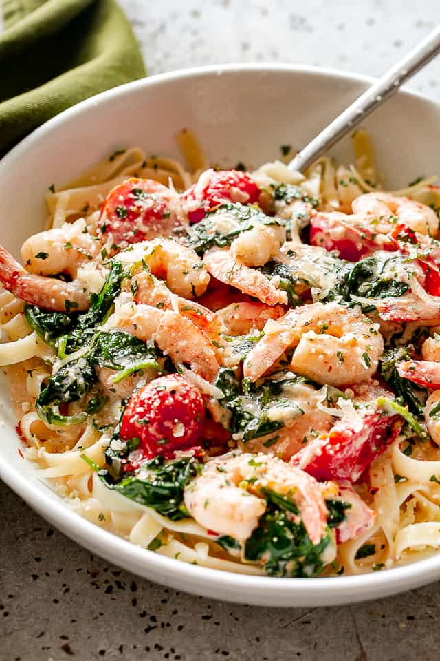 A large serving bowl of shrimp fettuccine with spinach and tomatoes.