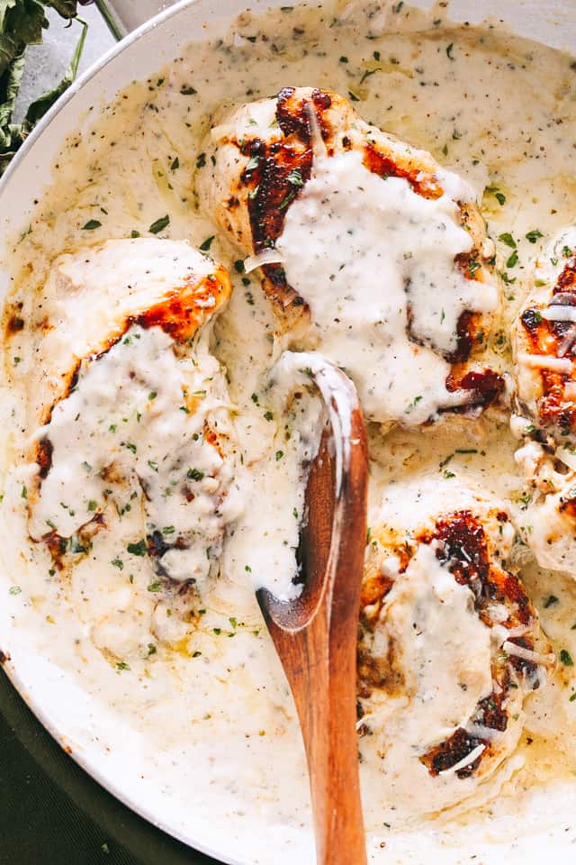 Overhead image of four chicken breasts cooking in a herby garlic cream sauce.