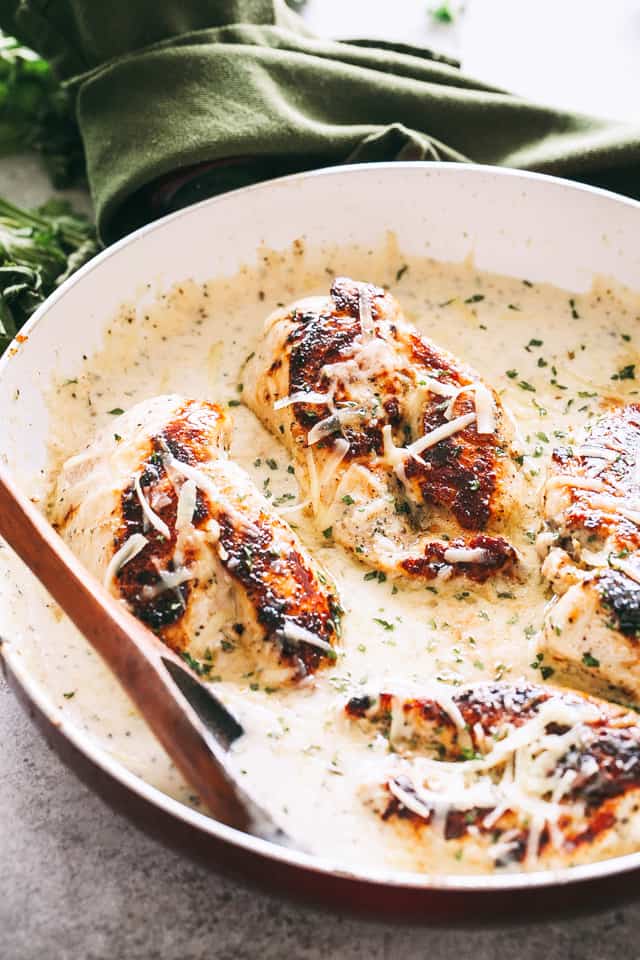 Four pan-seared chicken breasts cooking in a skillet with a cream sauce.
