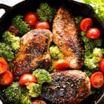 Overhead view of balsamic chicken breasts in a skillet surrounded by broccoli florets and halved grape tomatoes.