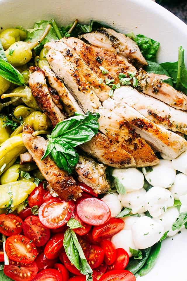 Antipasto Salad with Grilled Chicken and Basil Pesto Vinaigrette served in a white salad bowl.
