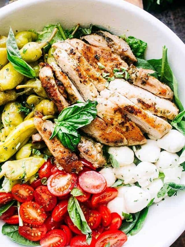 Overhead view of an antipasto salad with grilled chicken, tomatoes, fresh mozzarella, and pepperoncini in a white bowl.