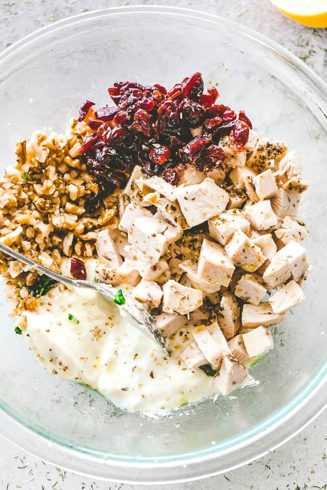 Chopped chicken, walnuts, cranberries, and mayo dressing in a glass mixing bowl.