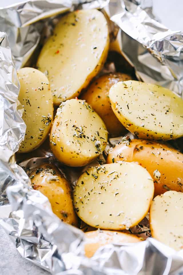 Halved small potatoes in foil packs, garnished with dried herbs.