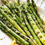 Grilled asparagus spears on a white plate garnished with lemon slices.