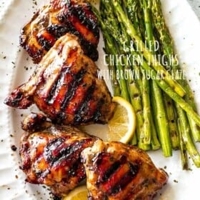 Overhead shot of Grilled Chicken Thighs with Brown Sugar Glaze arranged on a serving platter, with grilled asparagus placed next to the chicken thighs.