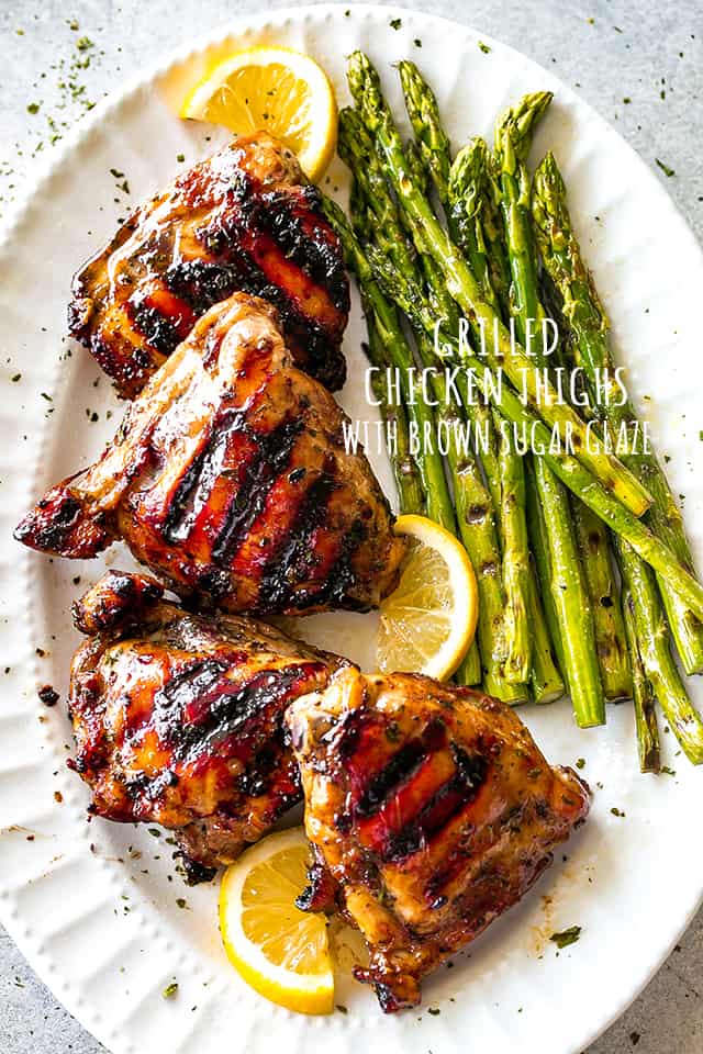 Overhead shot of Grilled Chicken Thighs with Brown Sugar Glaze arranged on a serving platter, with grilled asparagus placed next to the chicken thighs.