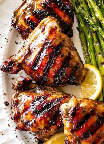 Overhead, close-up photo of Grilled Chicken Thighs with Brown Sugar Glaze arranged on a serving platter, with grilled asparagus placed next to the chicken thighs.
