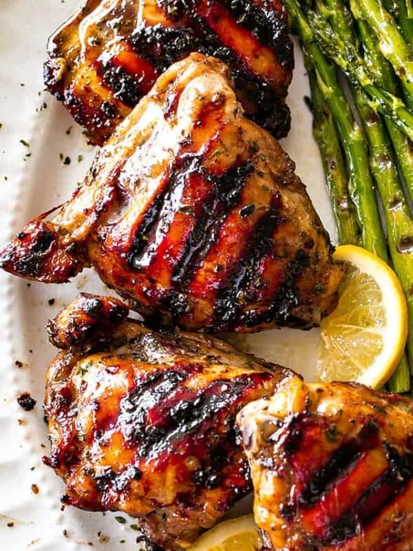 Overhead, close-up photo of Grilled Chicken Thighs with Brown Sugar Glaze arranged on a serving platter, with grilled asparagus placed next to the chicken thighs.