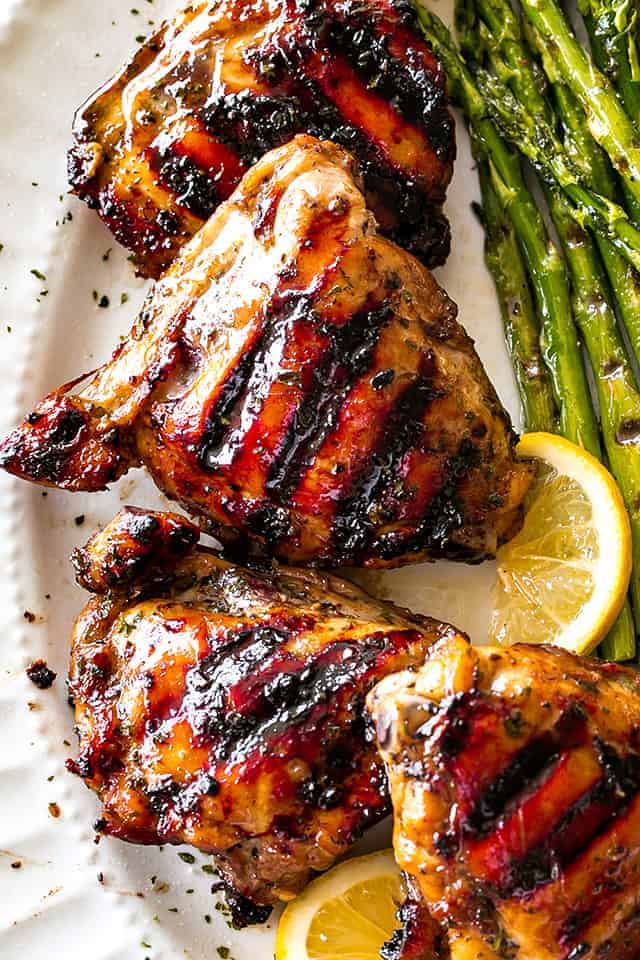 Overhead, close-up photo of Grilled Chicken Thighs with Brown Sugar Glaze arranged on a serving platter, with grilled asparagus placed next to the chicken thighs.