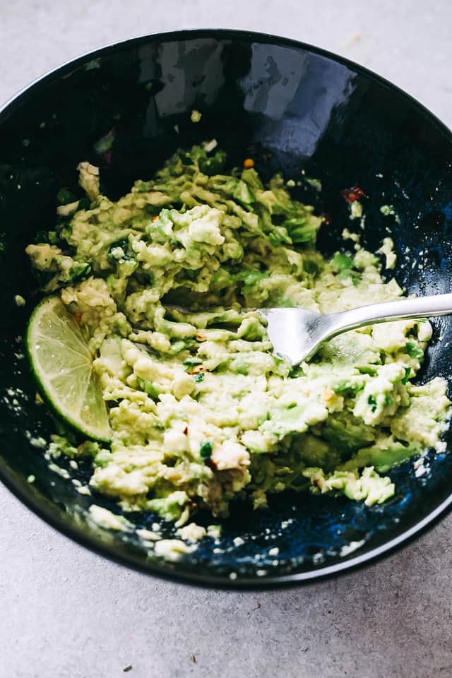 Fork smashing guacamole in bowl