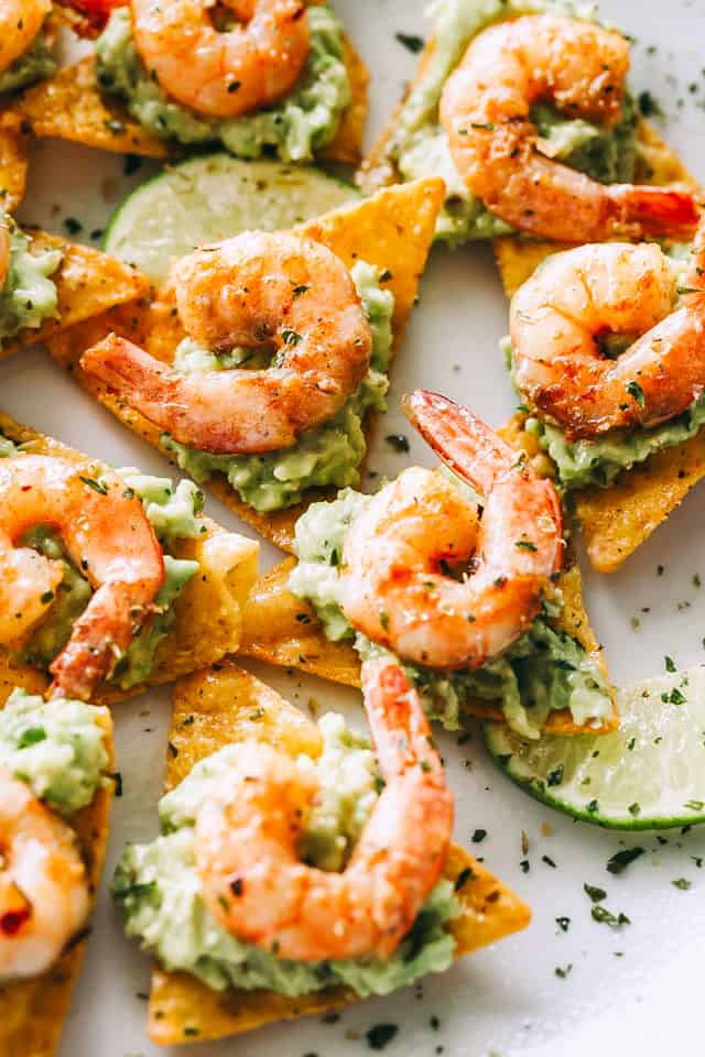 Overhead view of tortilla chips topped with guacamole and Cajun shrimp with lime wedges
