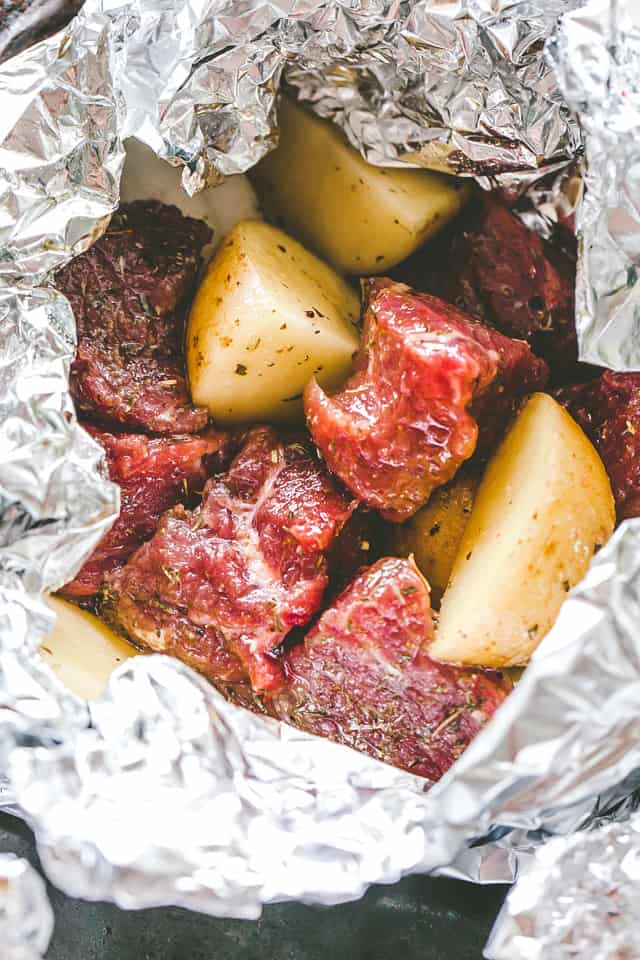 Uncooked garlic and herb steak and potatoes inside an open foil packet.