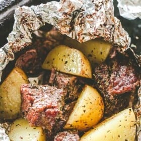 An open garlic and herb steak and potatoes foil packet.