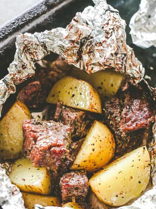 An open garlic and herb steak and potatoes foil packet.