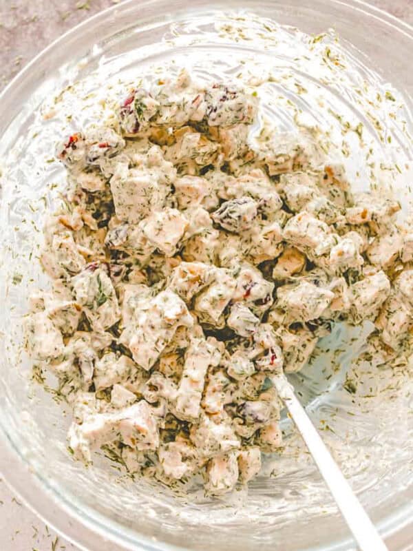 Making a Chicken Salad in a glass mixing bowl with nuts, cranberries, and creamy mayo dressing.