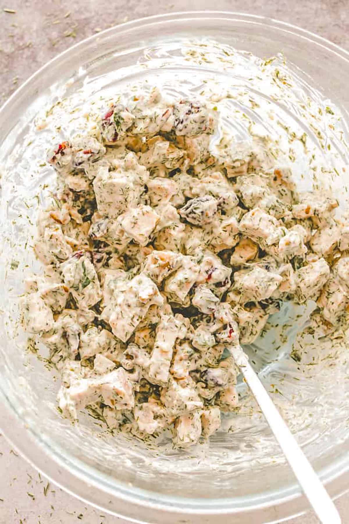 Making a Chicken Salad in a glass mixing bowl with nuts, cranberries, and creamy mayo dressing.