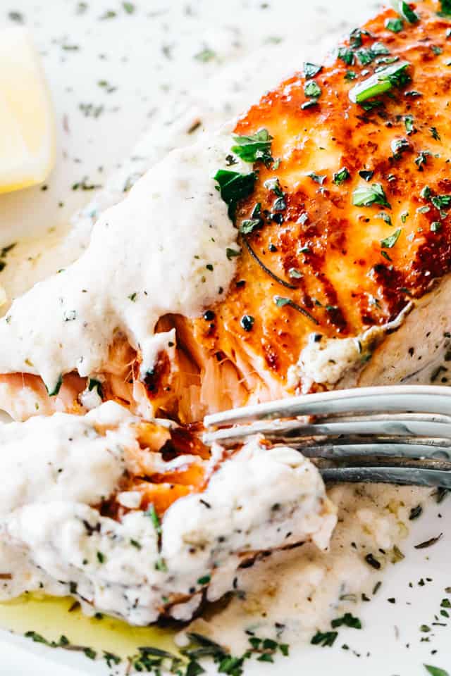 Close-up shot of a pan seared salmon fillet topped with white creamy sauce.