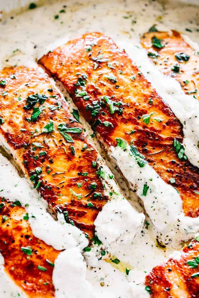 Fillets of salmon, pan-seared to a dark golden-brown, with a creamy sauce and chopped herb garnish.