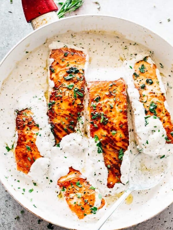 A skillet with four salmon fillets in a white cream sauce.