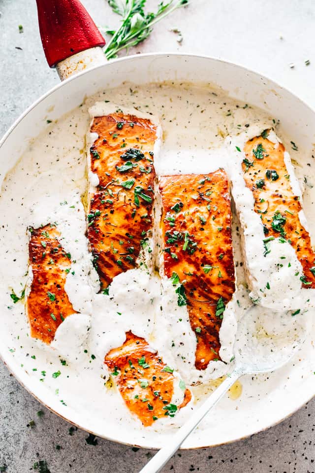 A skillet with four salmon fillets in a white cream sauce.