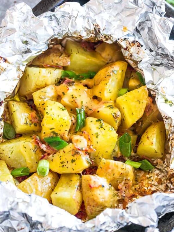 Grilled diced potatoes in a foil pack with bacon, cheese, and a garnish of green onions.