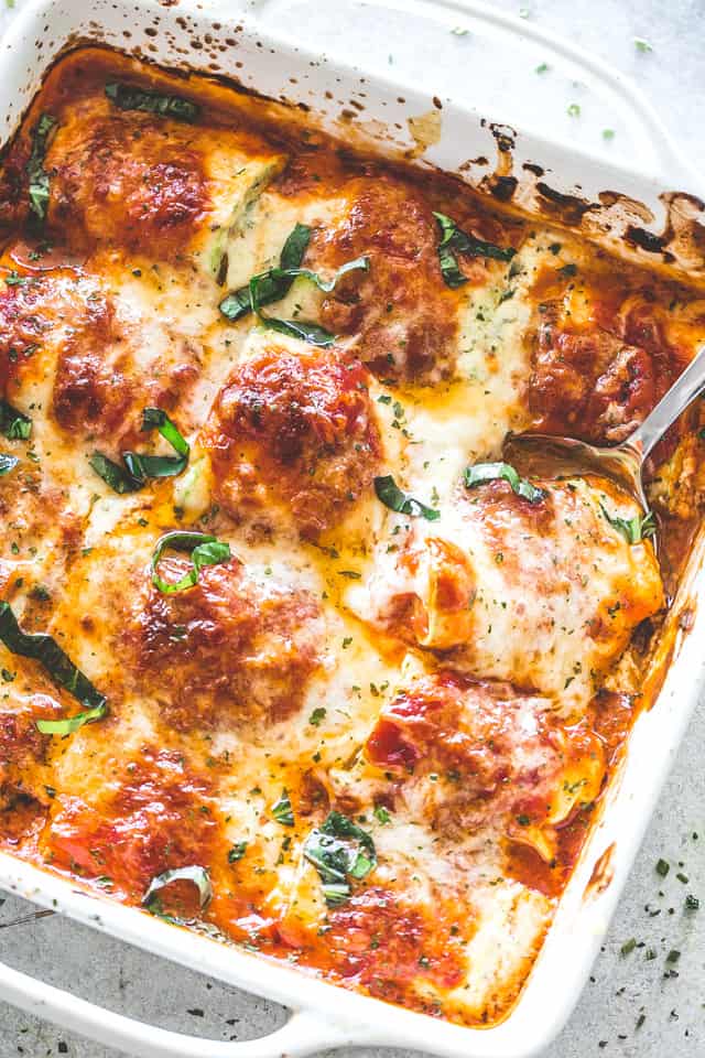 Overhead photo of zucchini lasagna roll ups in a dish with a spoon taking one bundle out of the baking dish.