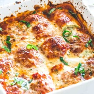 Zucchini lasagna roll ups arranged and baked in a white baking dish.