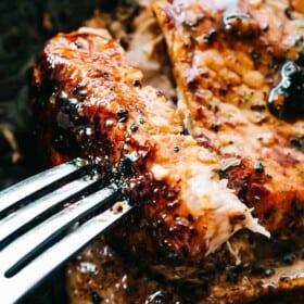Close up of a fork stuck into a baked honey garlic pork chop on a sheet pan.