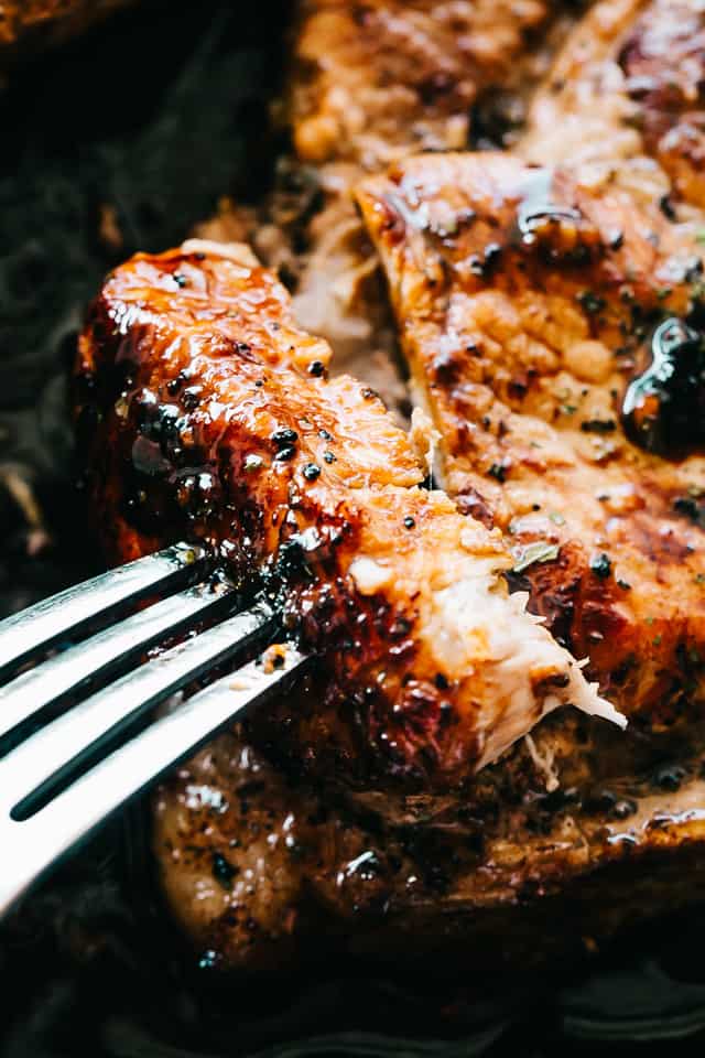 Close up of a fork stuck into a baked honey garlic pork chop on a sheet pan.