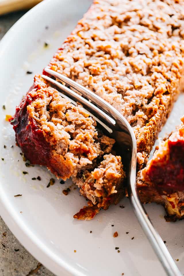 A fork cutting into a slice of homemade meatloaf on a white plate