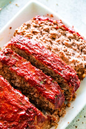 A sliced meatloaf with tomato glaze on a white serving plate.