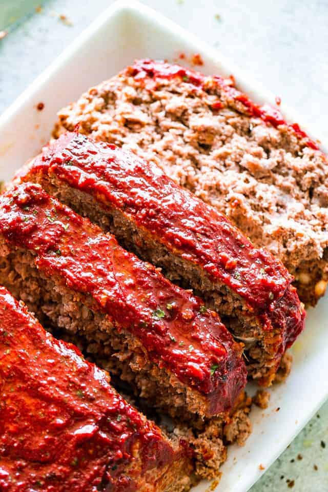 A sliced meatloaf with tomato glaze on a white serving plate.