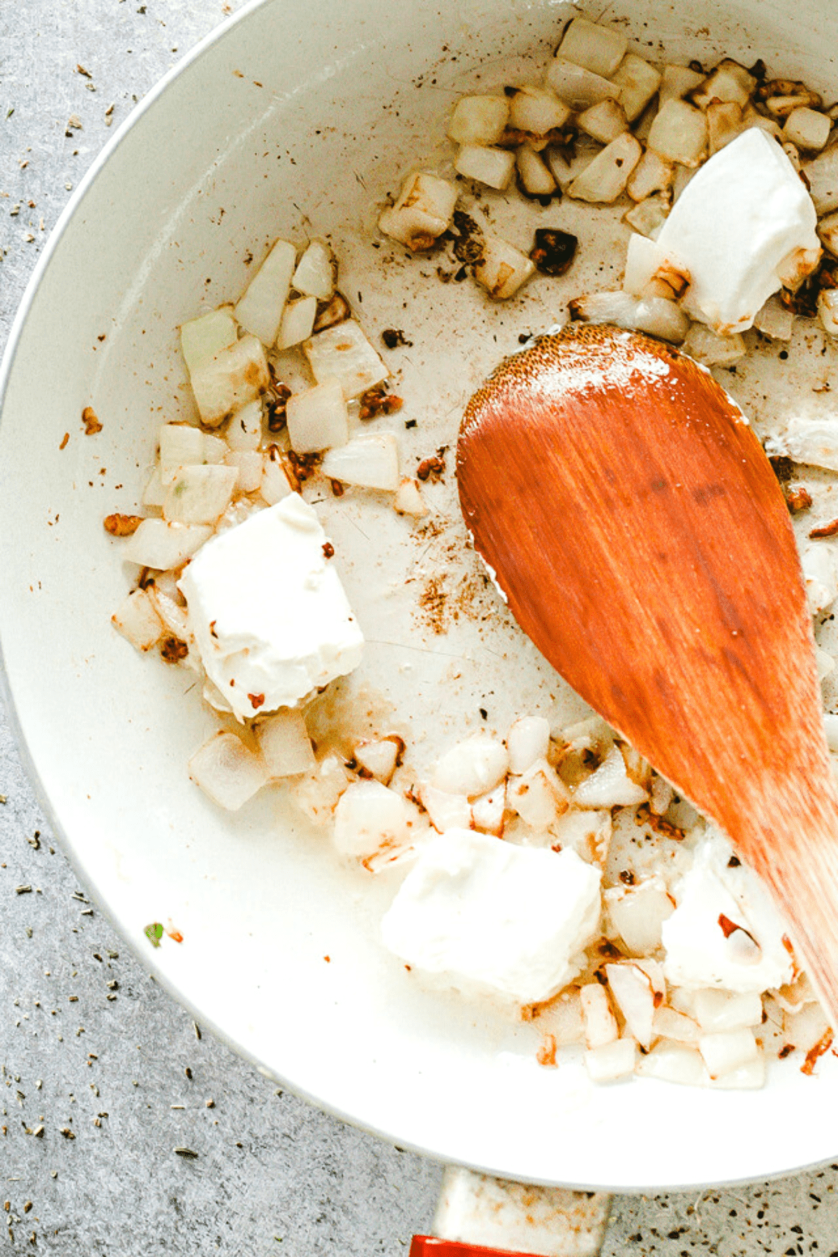 wooden spoon stirring through cream cheese and onions in a skillet.