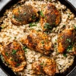 a skillet with cooked garlic butter chicken with rice and garnished with parsley.