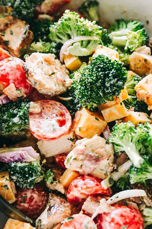 Close up photo of broccoli florets, halved cherry tomatoes, cubed chicken, and sliced red onions.