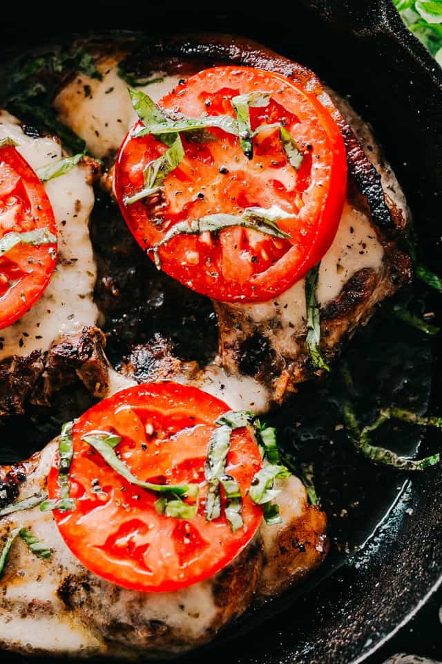 Overhead, close-up photo of Caprese Pork Chops - seared pork chops topped with melted mozzarella, tomato slices, and fresh basil ribbons.