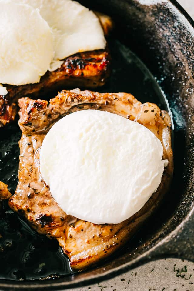Close-up image of seared pork chops topped with fresh mozzarella cheese slices.