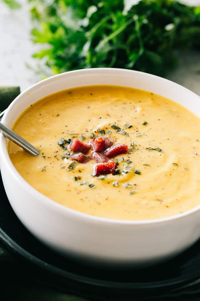 Cauliflower Cheese Soup served in a white bowl and garnished with diced bacon and dried chives.