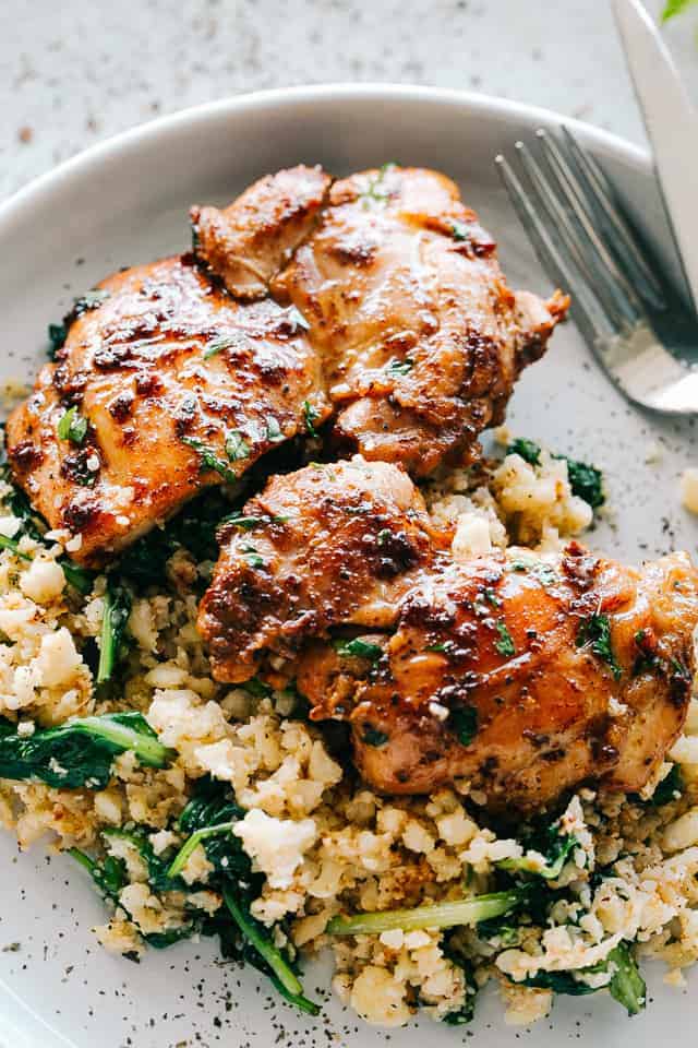 cooked chicken thighs placed on a bed of cauliflower rice mixed with baby spinach.