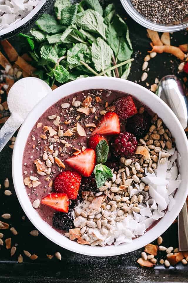 Overhead view of a berry smoothie bowl topped with fresh fruit, seeds, and shaved coconut.