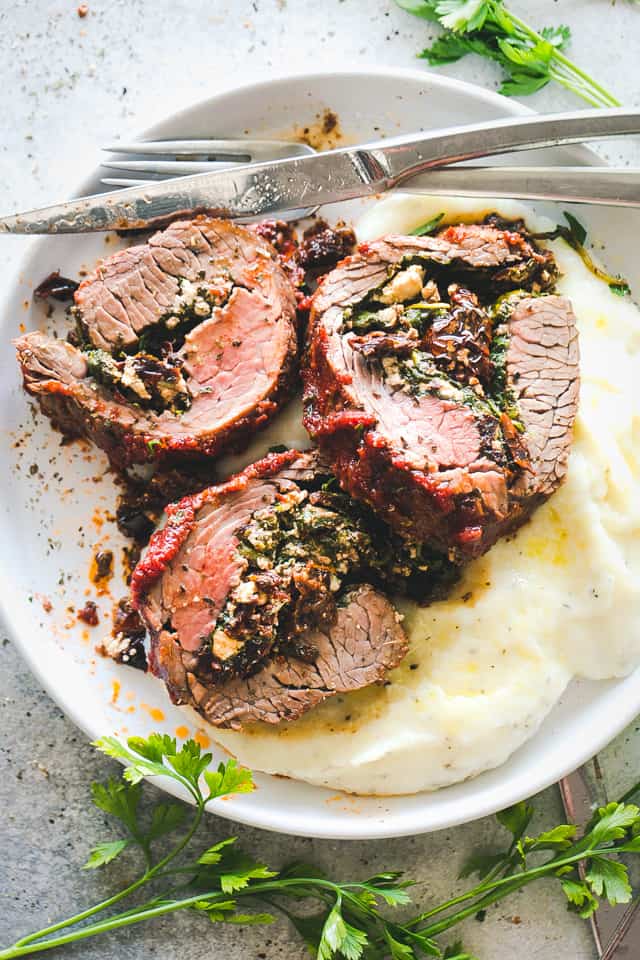 Stuffed flank steak served over a bed of mashed potatoes on a plate.