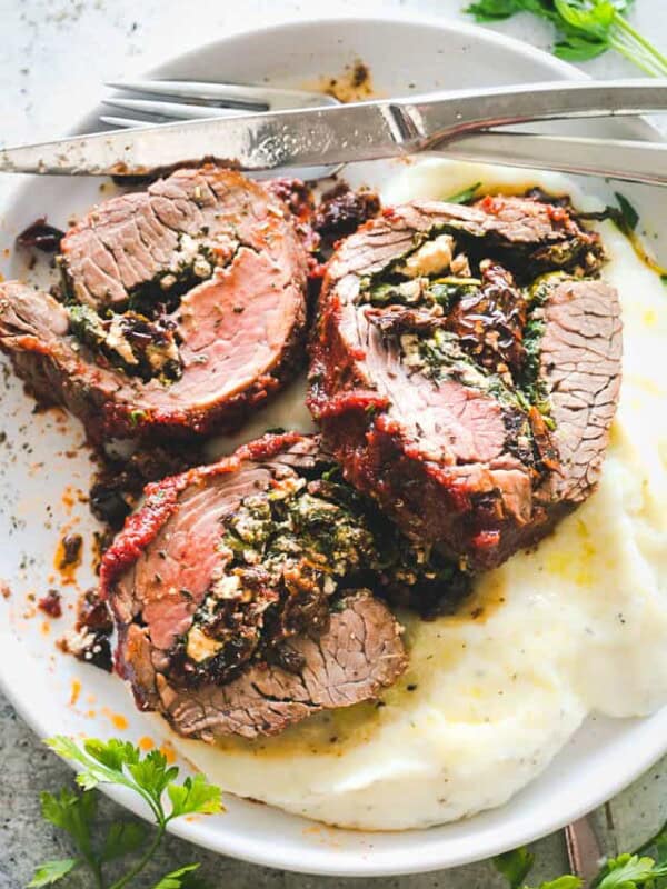 Stuffed flank steak served over a bed of mashed potatoes on a plate.