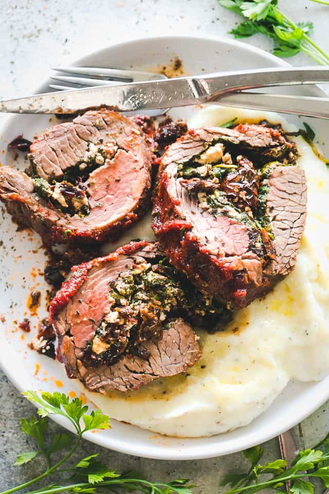 Stuffed flank steak served over a bed of mashed potatoes on a plate.