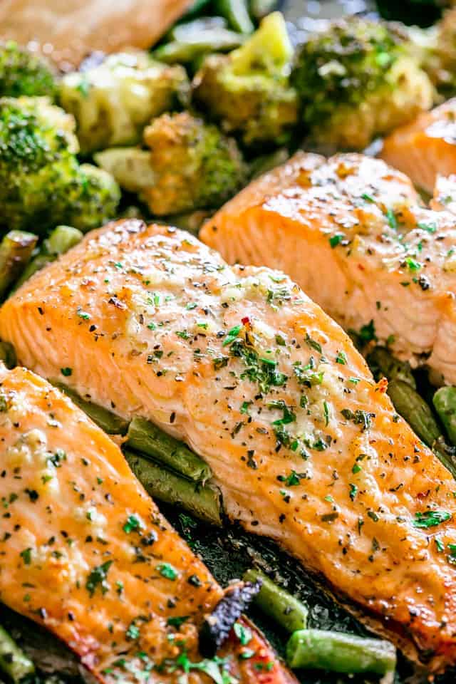 Seasoned salmon fillets baked on a sheet pan over a bed of green vegetables.