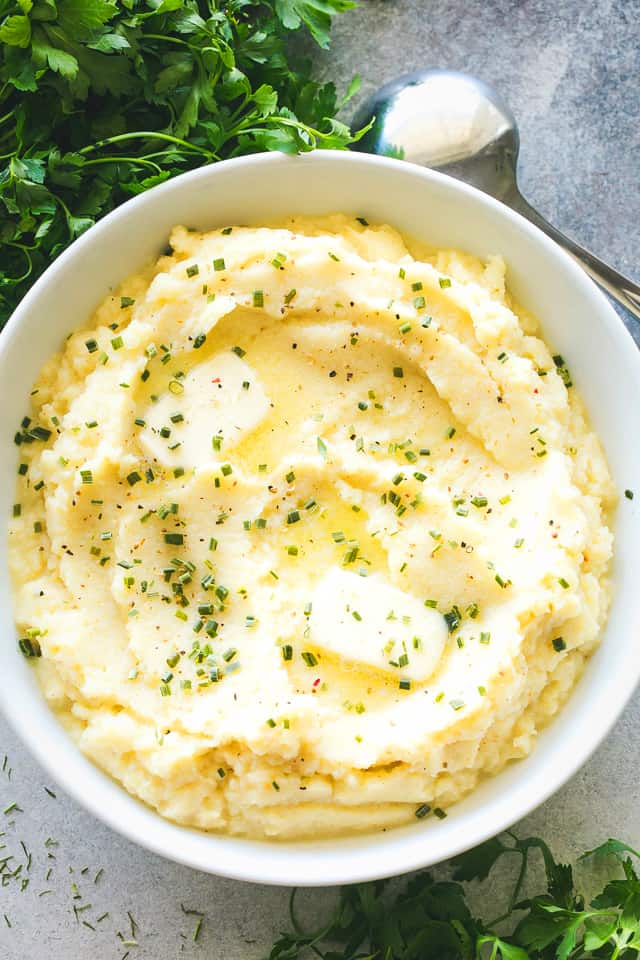 Overhead shot of a bowl with cauliflower mash garnished with pats of butter and chives.